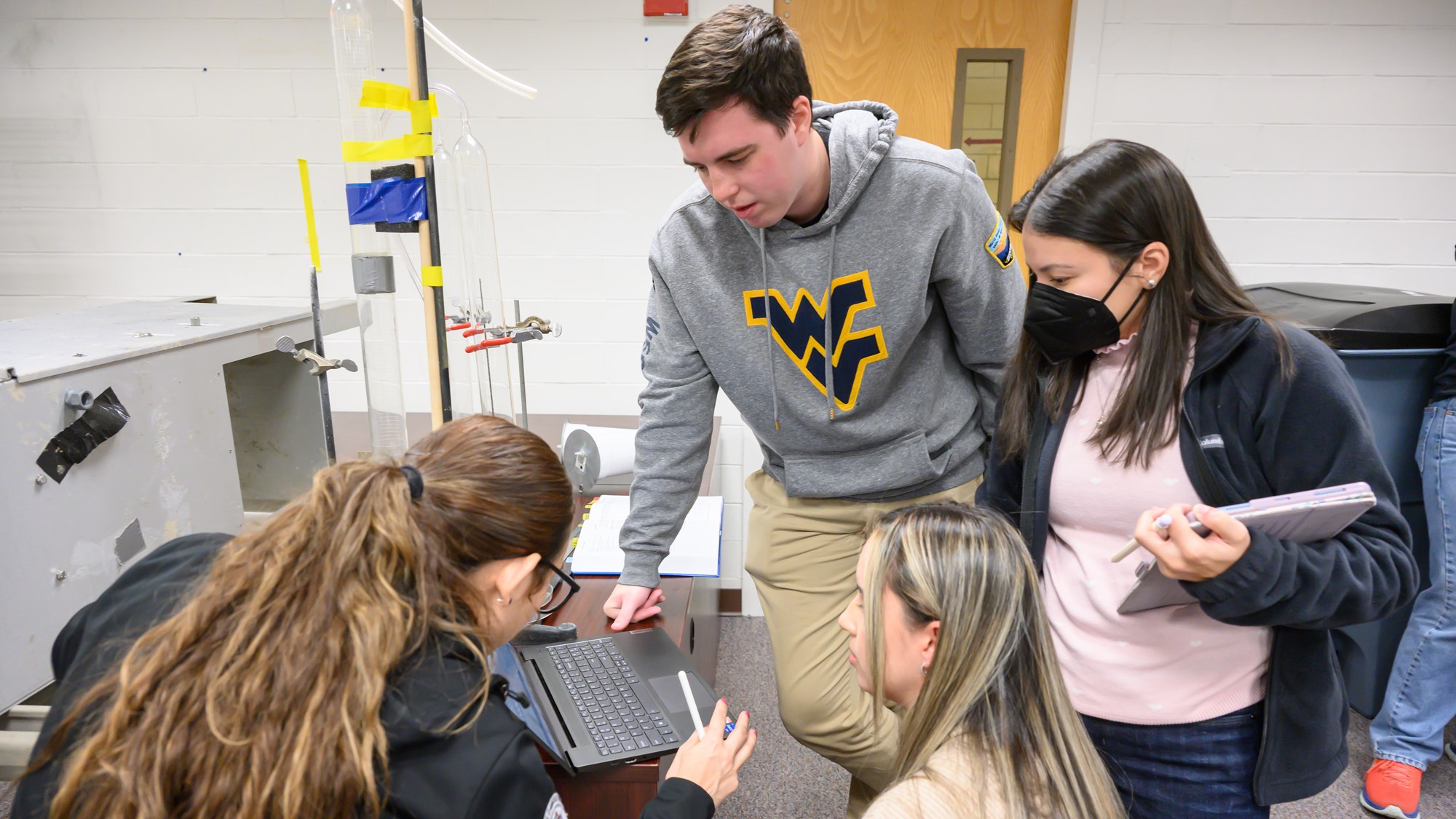 Four graduate students reviewing data on a laptop in an industrial hygiene ventilation workshop lab 