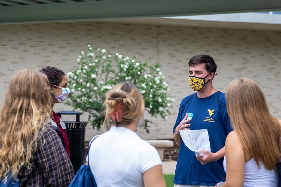 A group of students stand outside as fellow Public Health student Ryan Titus, wearing a Student Association of Public Health navy blue t-shirt, speaks to them