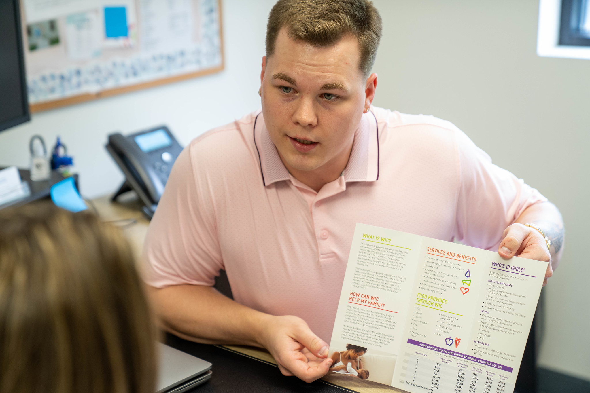 Male student sharing Women Infant Children informational brochure with patient in clinic setting. 