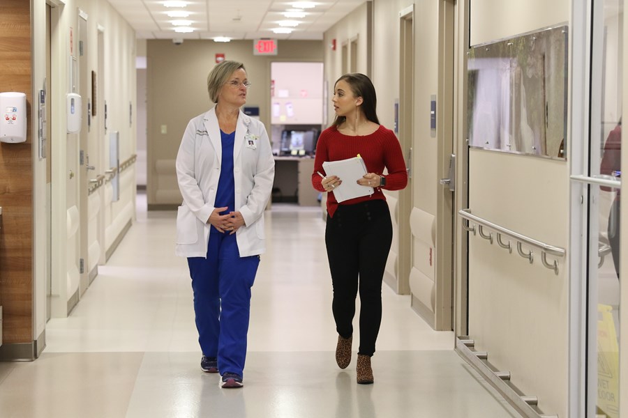 Healthcare worker and student walking down hall of hospital.