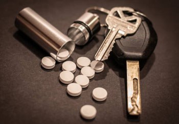 Picture of car keys lying next to a silver vial containing unknown pills