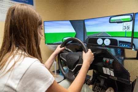 A close up of a blonde student using the simulator.  The screens a re showing a driving environment up close.