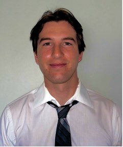 Smiling male wearing a white dress shirt with black and gray striped tie.